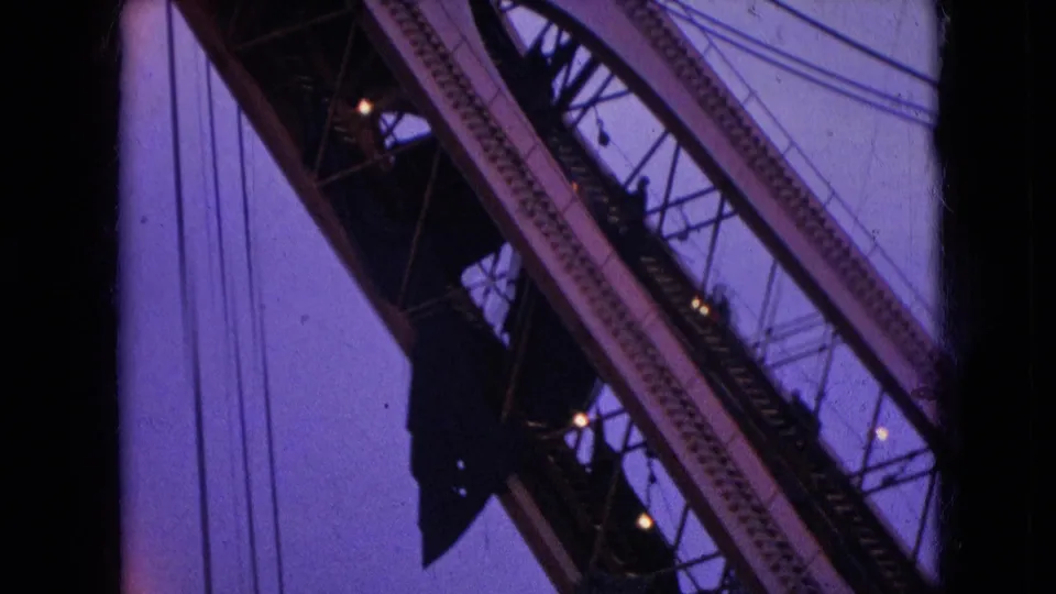 1966 Athens, Ohio 8mm frame with a close upward view of crane girders, cable lines, and dark pulley hardware set against the twilight sky.