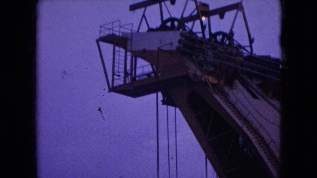 Low-angle 1966 Athens, Ohio 8mm frame showing the upper section of a large steel industrial structure with cables, railings, ladders, and a purple dusk or night sky.