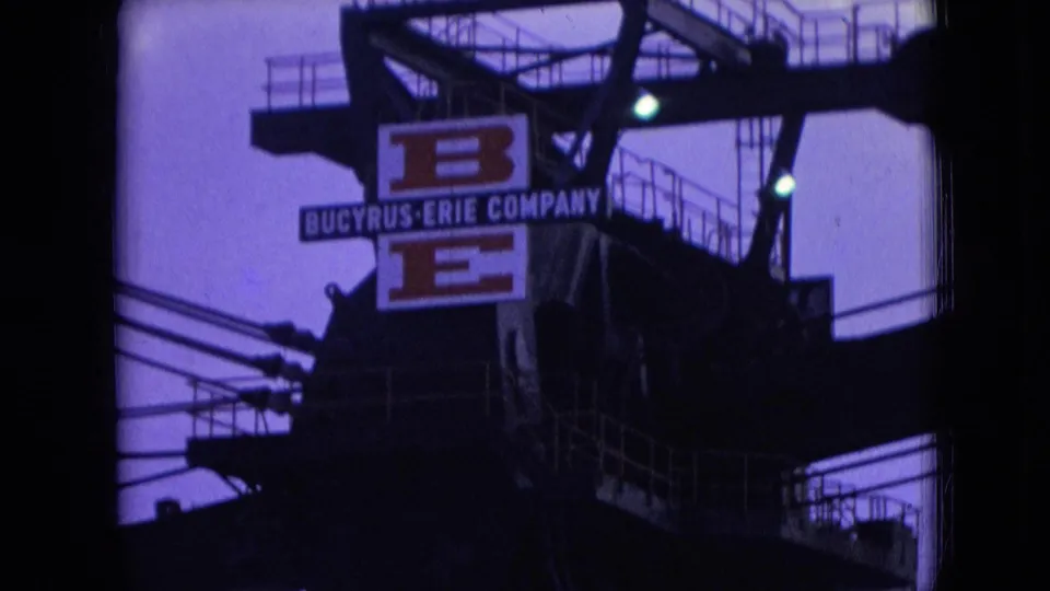 1966 Athens, Ohio frame showing the Bucyrus-Erie Company sign on a large steel industrial structure, with catwalk railings, small greenish lights, and overhead wires visible around it.