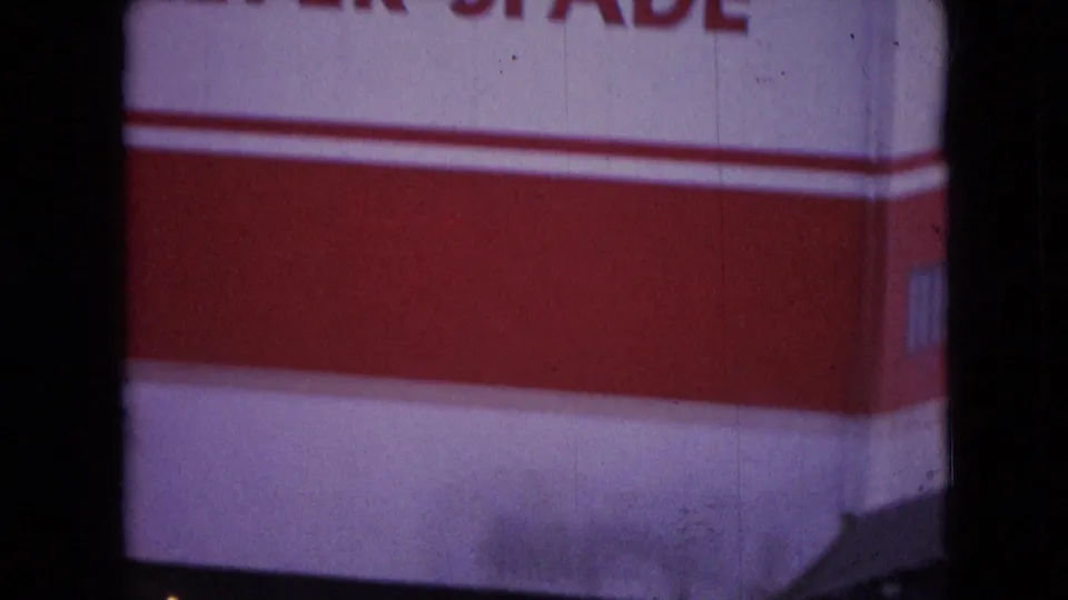 1966 Athens, Ohio home-movie frame showing the red-and-white side of industrial machinery with partial large The Silver lettering and dark film-frame shadows.
