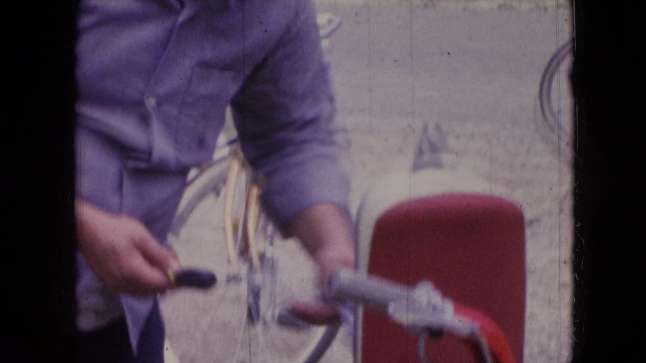 Man handles a small part near a bicycle and red scooter handlebar.