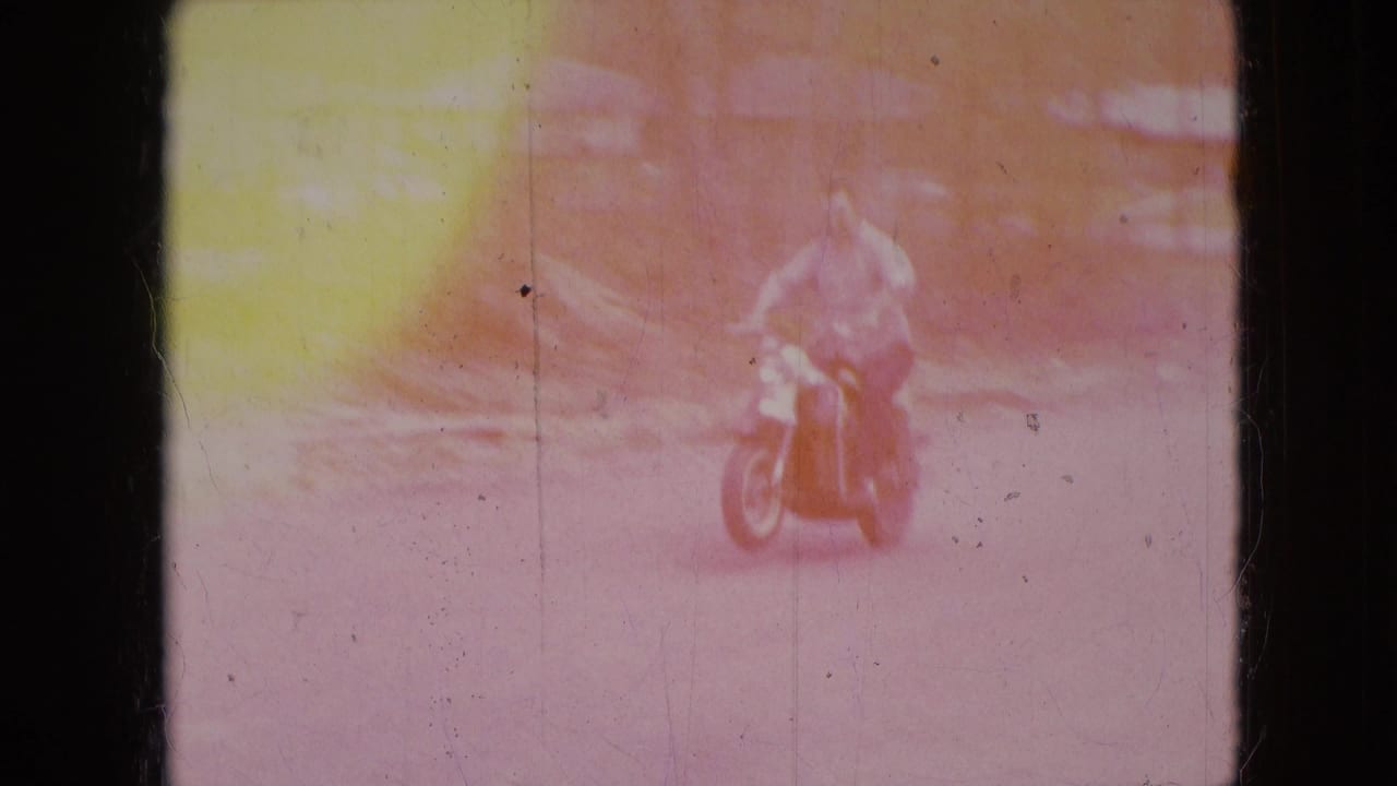 In 1966 home-movie footage from Athens, Ohio, a man on a red scooter approaches on a rural road through heavy color fading and film wear.