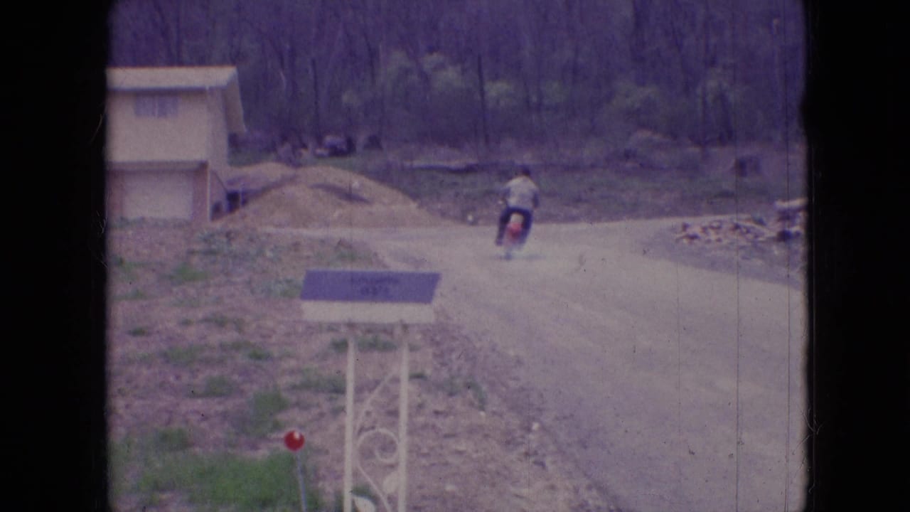 Motorcycle rider continues farther down the curving road past a small structure.
