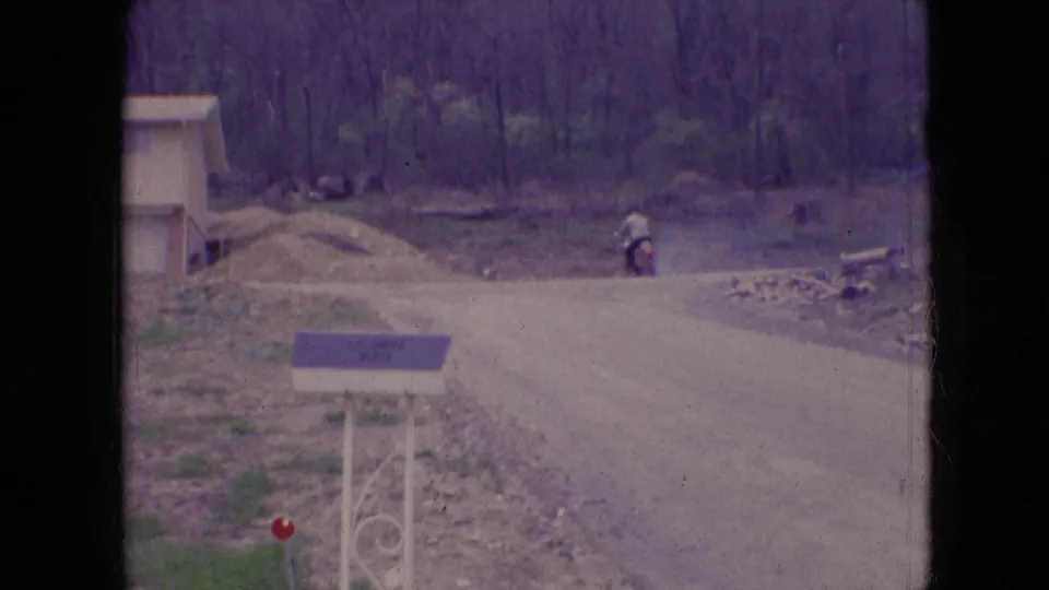 At the end of the short 1966 Athens, Ohio shot, the motorcycle rider is far down the unpaved road, framed by trees, roadside dirt, and the foreground mailbox.