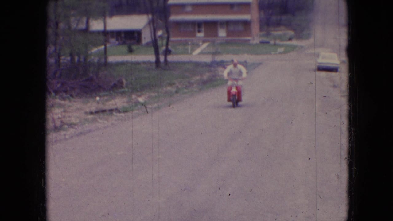 Man on a red moped riding toward the camera on a residential road.
