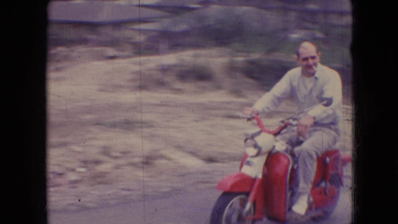 In Athens, Ohio home-movie footage from 1966, an adult man in pale clothing rides a red moped or small motorbike toward the camera on a country road.