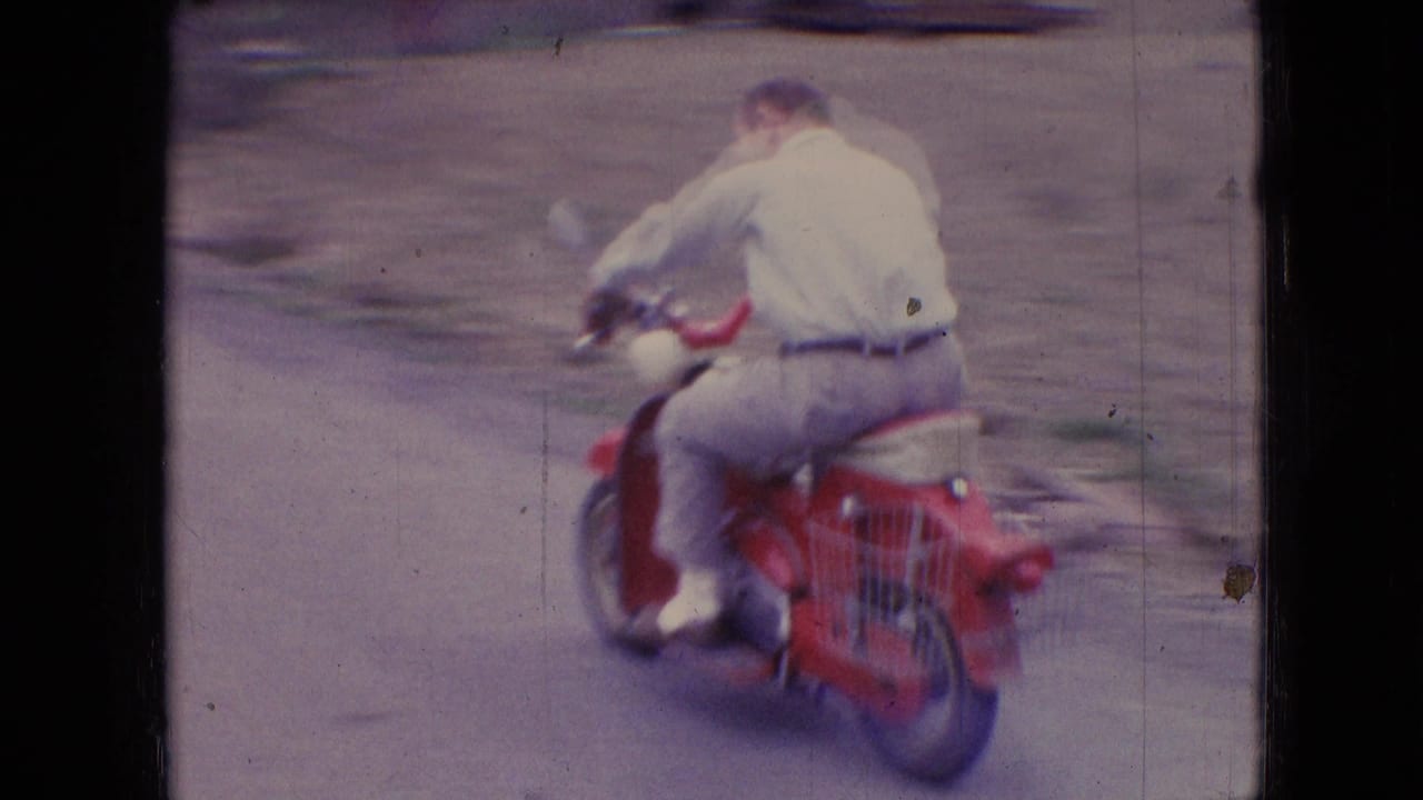 Man rides a red moped away from the camera along a curving rural road.