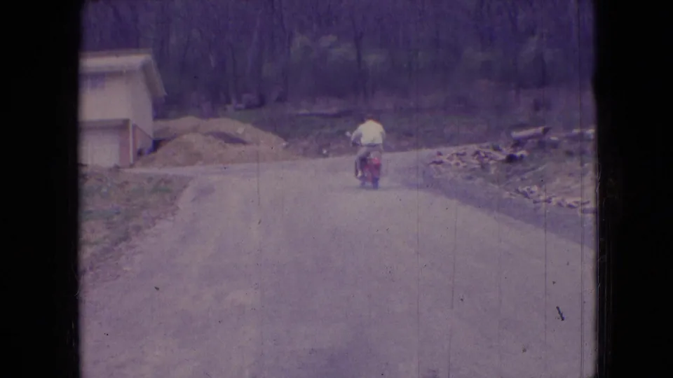 The final frame shows the rider farther away on the red moped, with a small roadside building and wooded background visible along the rural Athens, Ohio road.