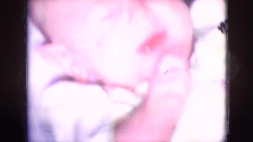 A brief overexposed 8mm frame shows soft pale and pink shapes with little identifiable detail.