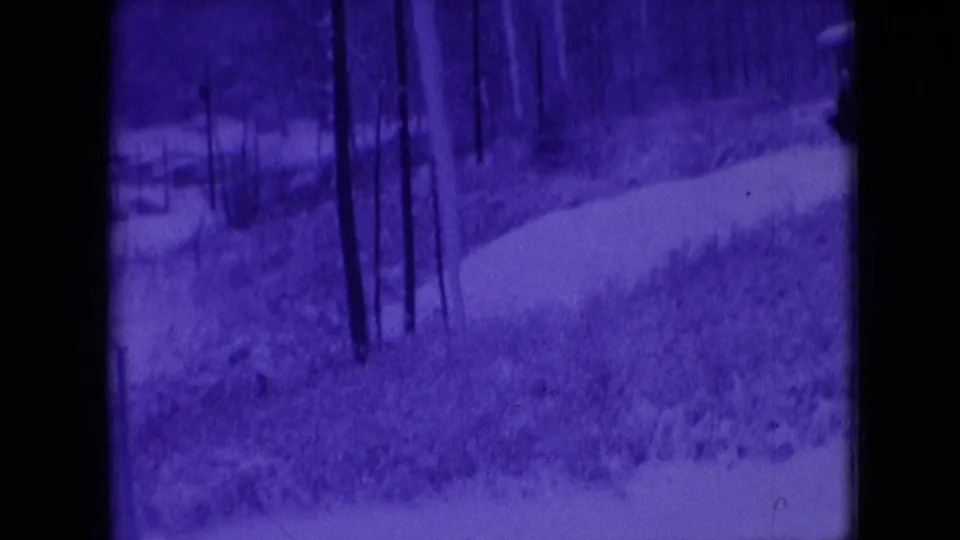 Blue-tinted winter landscape from the Athens, Ohio home movie, with a curved snow path, leafless trees, and brush visible in soft 8mm texture.