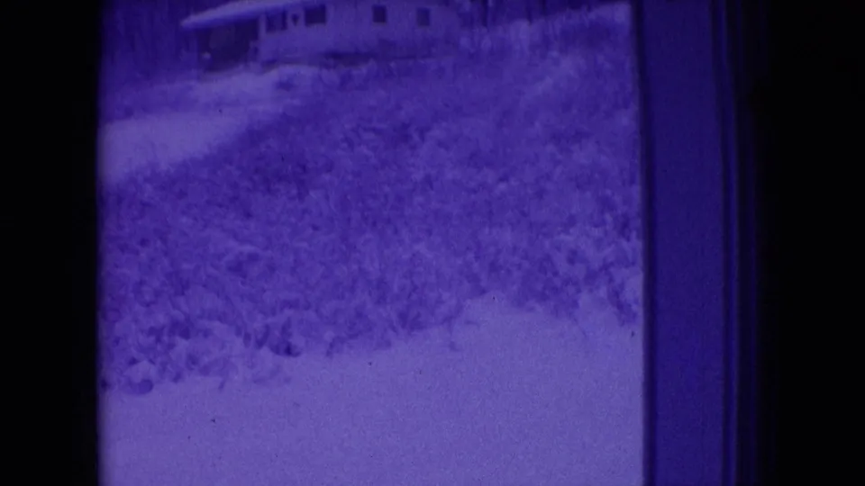 Blue-tinted 1966 Athens, Ohio home-movie frame with a distant house above snow-covered brush and yard, bordered by dark 8mm gate edges.