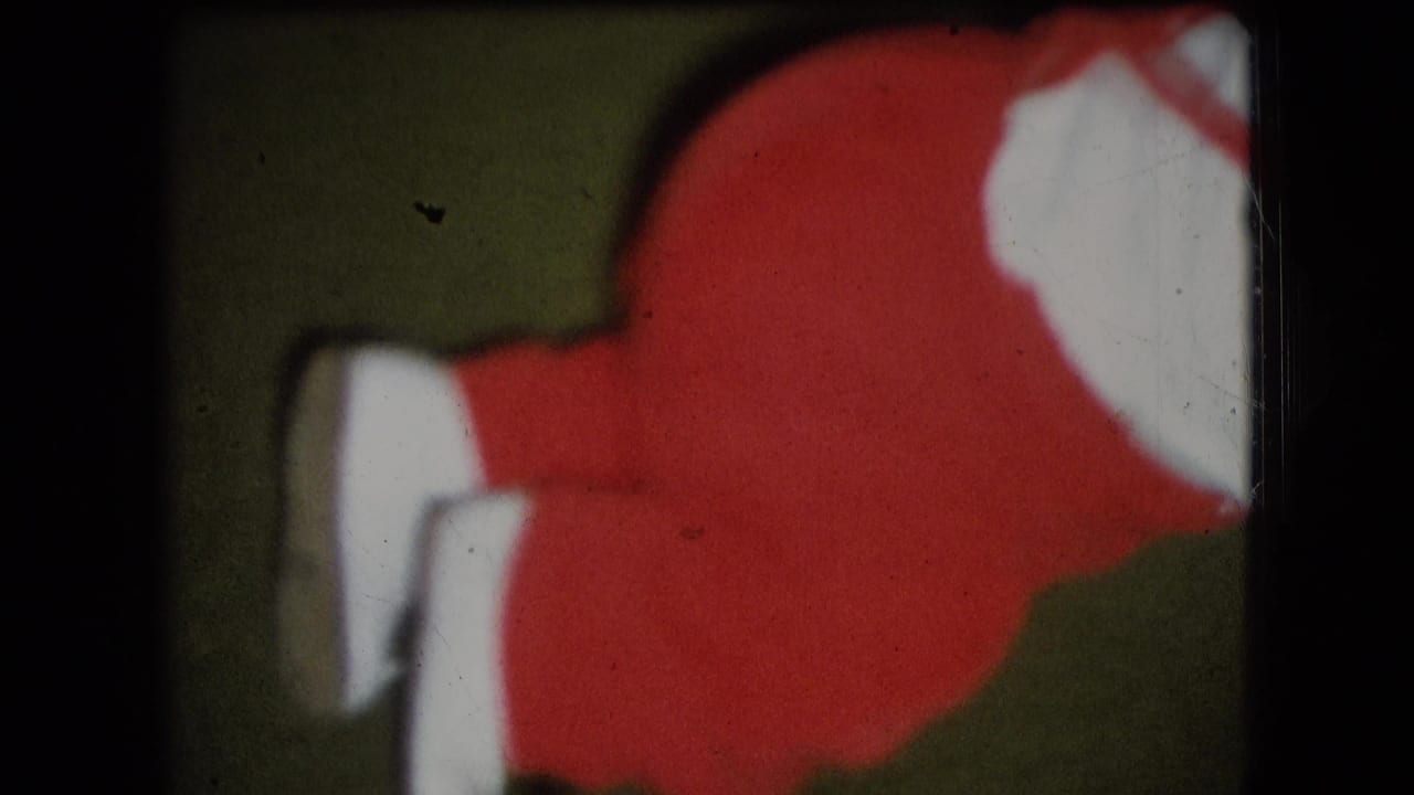 Close 1966 home-movie frame from Athens, Ohio showing the lower half of a small child in red clothing with white shoes on a green carpeted floor.
