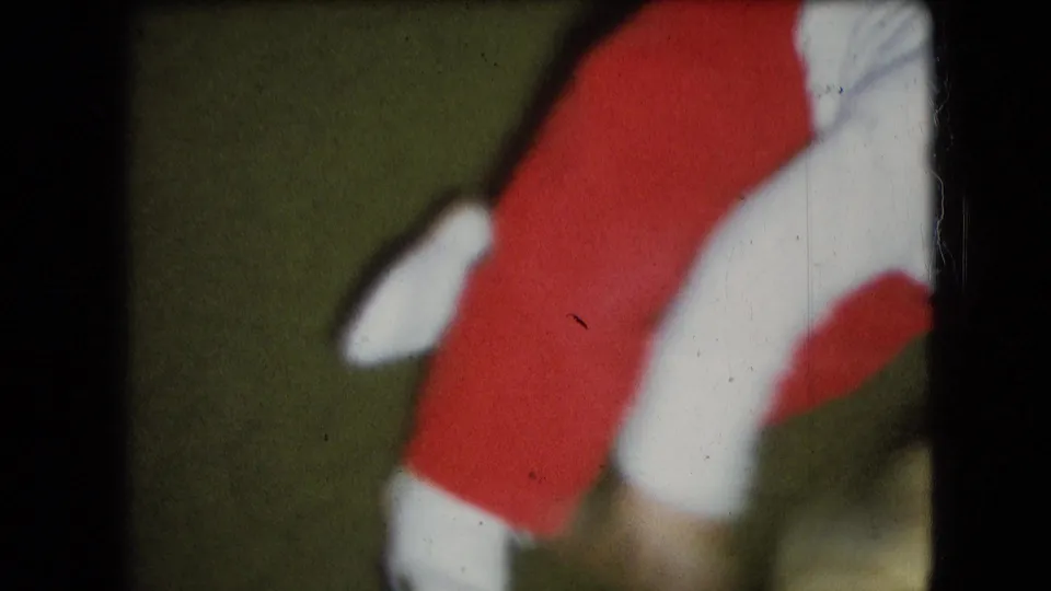 Close-cropped 1966 Athens, Ohio home-movie frame showing a small child’s lower body in red clothing and white shoes while moving on a green floor.