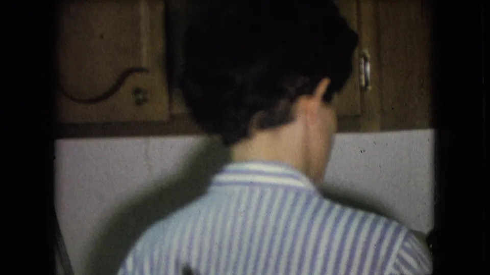 A closer home-movie view shows the back of the striped shirt as the person works near the sink beneath wood wall cabinets in the Athens, Ohio kitchen.