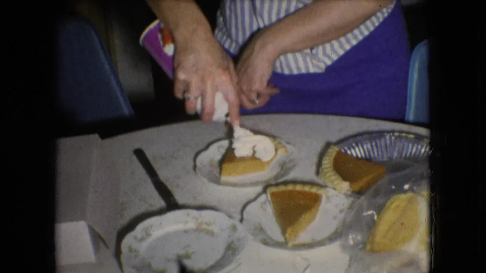 In the 1966 home kitchen scene, the woman tops a slice of sweet potato pie with whipped cream while other pie slices and tableware sit nearby.