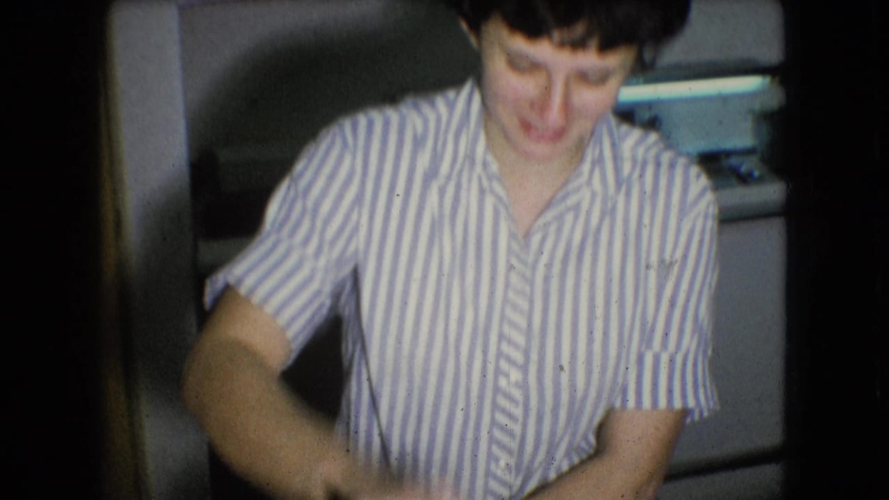 Woman in a striped shirt looks down while seated or standing near a kitchen table.