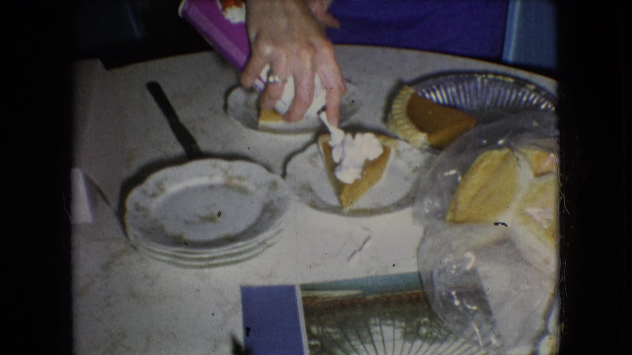 In 1966 Athens, Ohio home-movie footage, a woman's hands place whipped cream on pumpkin pie slices beside stacked plates, a whole pie, and wrapped bread on a kitchen table.