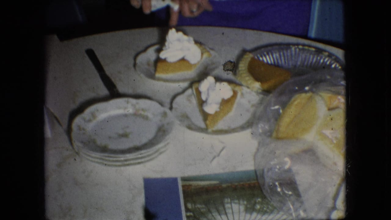 Pumpkin pie slices with whipped cream sit on paper plates beside a whole pie and stacked dishes.