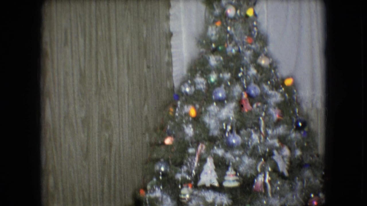 Decorated Christmas tree with tinsel, colorful ornaments, and small lights inside a wood-paneled Athens, Ohio home documented as 1966 8mm footage.