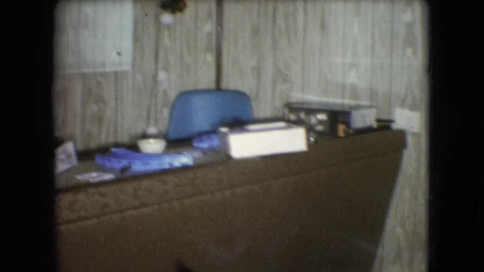 Closer view of a domestic desk or counter with a blue chair, papers, a small bowl, and containers in the reported 1966 Athens, Ohio home interior.
