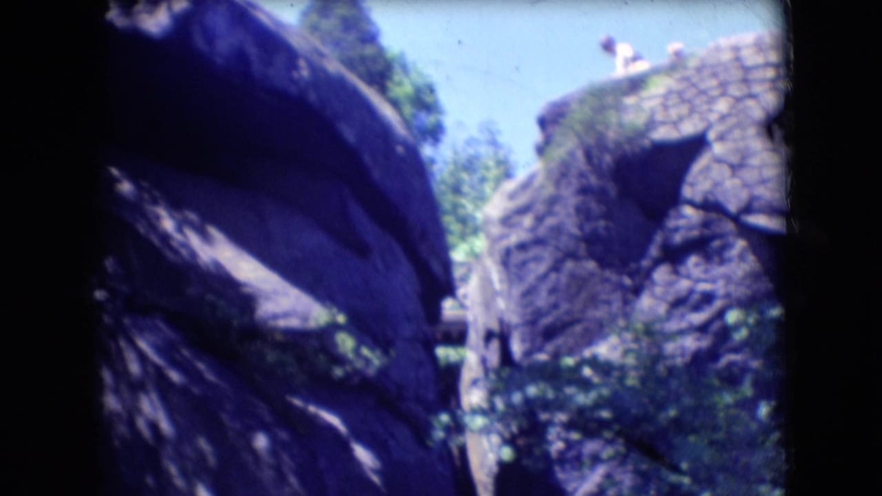 Large rock formations and leafy trees appear in this 1966 Athens, Ohio 8mm home-movie frame, with dark film borders and soft focus.