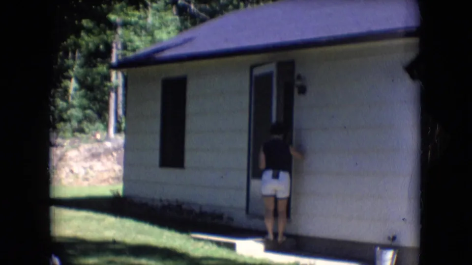 The woman is at the doorway of the small cabin, with grass, trees, and a light exterior wall visible in the final 1966 Athens, Ohio frame.