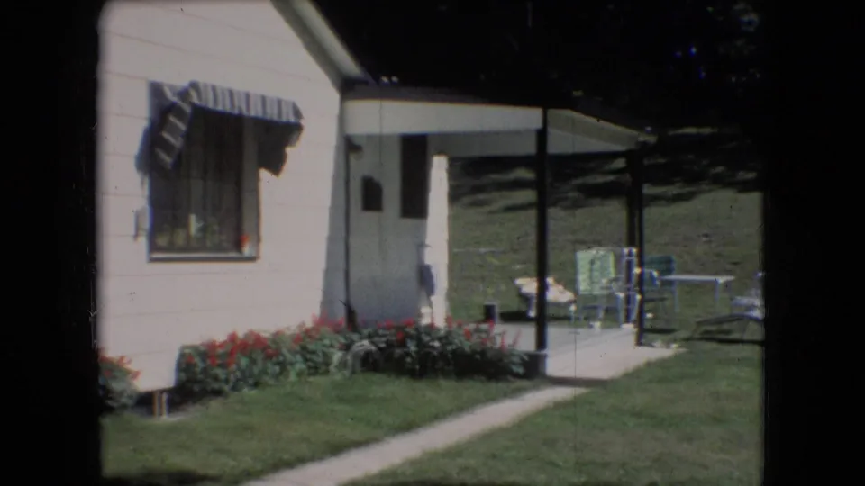 1966 Athens, Ohio home-movie frame showing a residential exterior with a flower bed, walkway, shaded porch cover, lawn, and outdoor patio furniture.