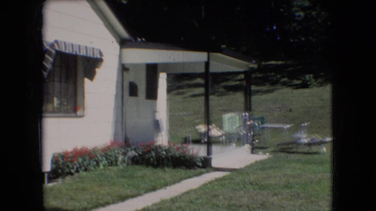 1966 Athens, Ohio home-movie frame showing a white-sided house with a striped awning, red flowers, green lawn, concrete walkway, and outdoor chairs.