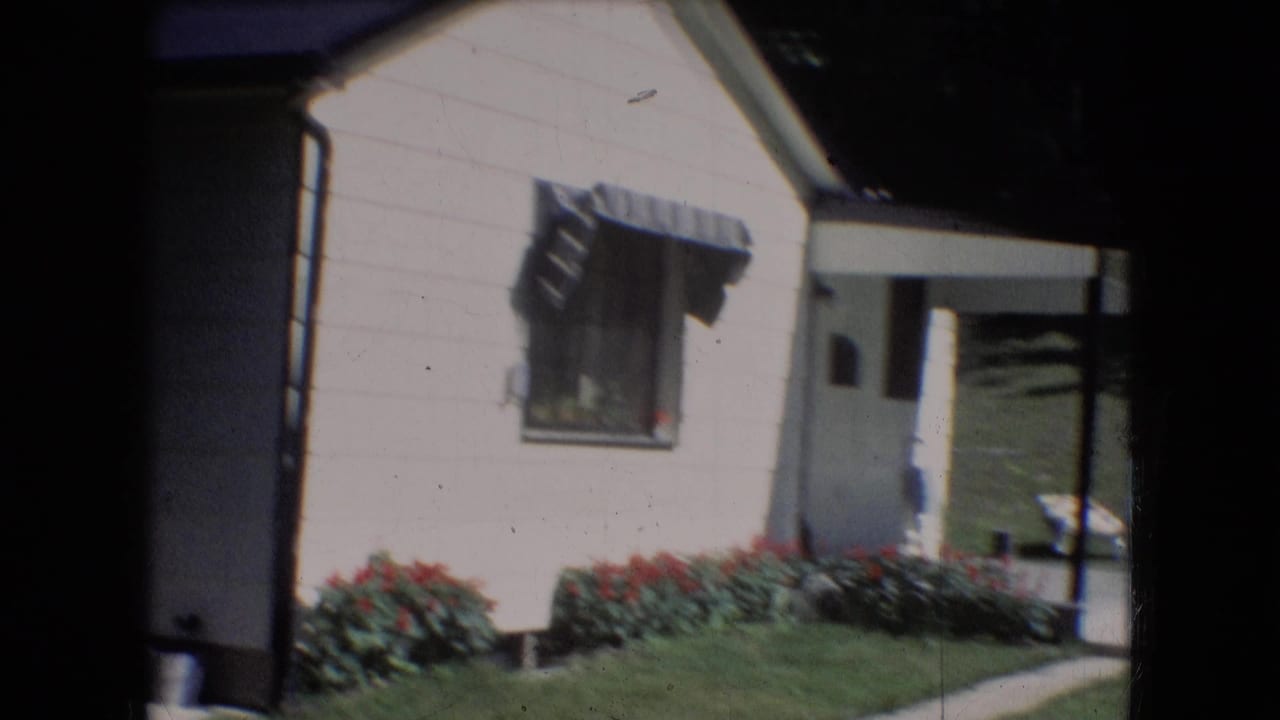 1966 Athens, Ohio frame of the house exterior with a striped window awning, red flowers along the wall, lawn, and a shaded doorway area.