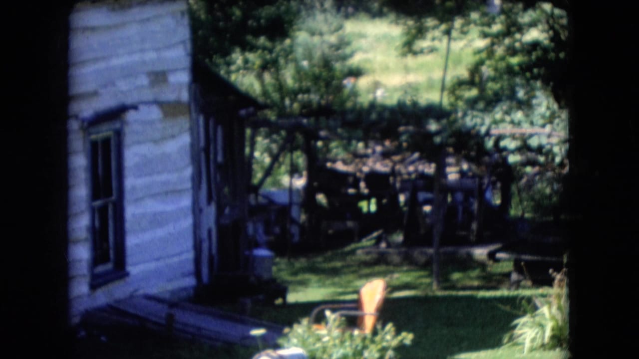 1966 Athens, Ohio 8mm frame showing a weathered white-sided structure, shaded yard, trees, and adjacent backyard elements with heavy frame-edge shadow.