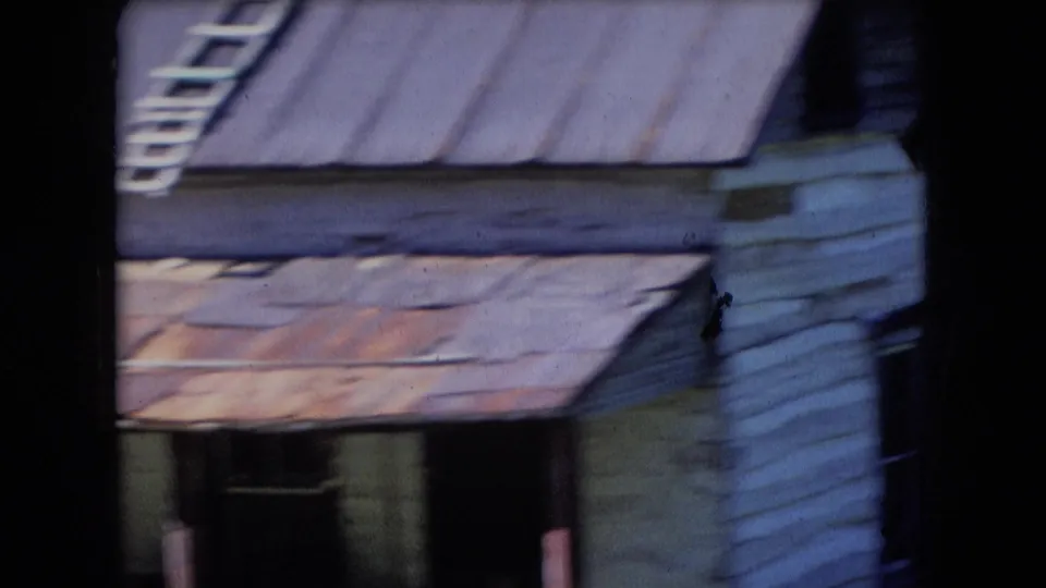 Athens, Ohio 1966 8mm frame showing a close view of a weathered white house or cabin with rusted metal roofing and shaded porch details.