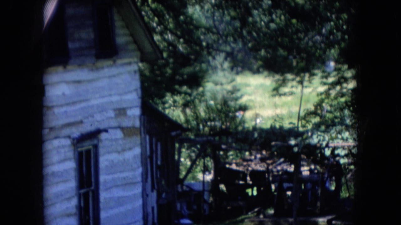 Athens, Ohio 1966 8mm frame showing the side wall of a weathered white house with trees, grass, and a shaded outdoor structure in the yard.