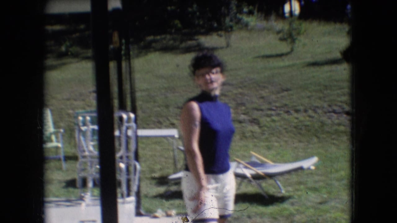 The woman stands near dark glass-door framing in a 1966 Athens, Ohio backyard scene, with metal lawn chairs, a lounge chair, and grass visible behind her.