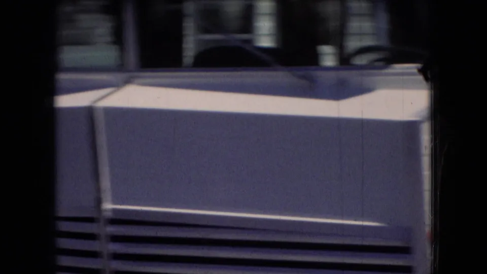 End-of-clip 8mm frame from the Athens, Ohio reel, partly obscured by film-gate darkness, showing a light-colored rectangular object or structure with horizontal slats as the pond shot transitions away.
