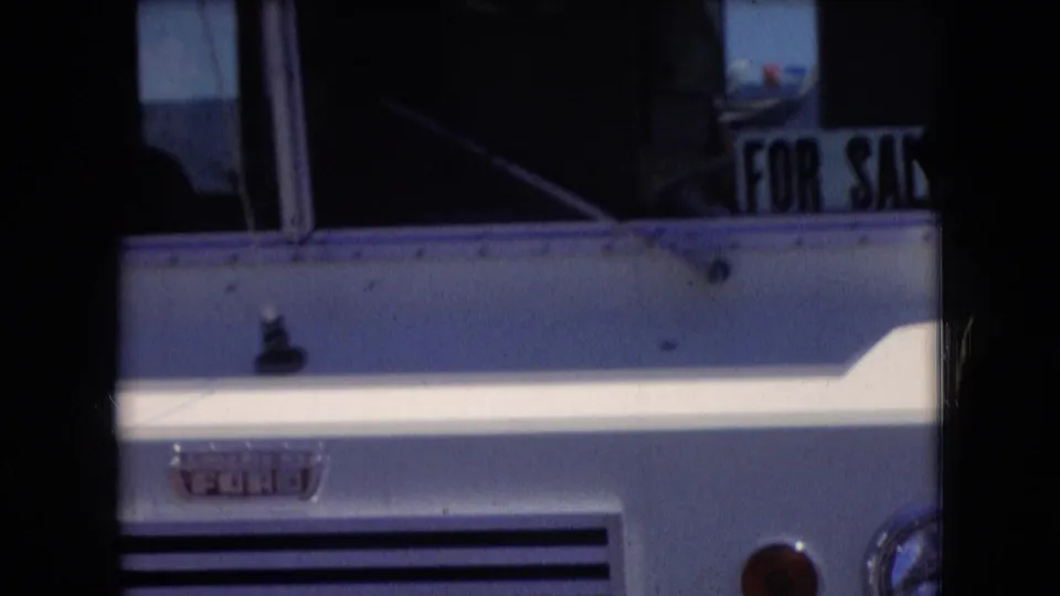 Athens, Ohio 1966 frame showing the RV front corner and side window area, with the grille, white bodywork, blue trim, and partial branding still visible.