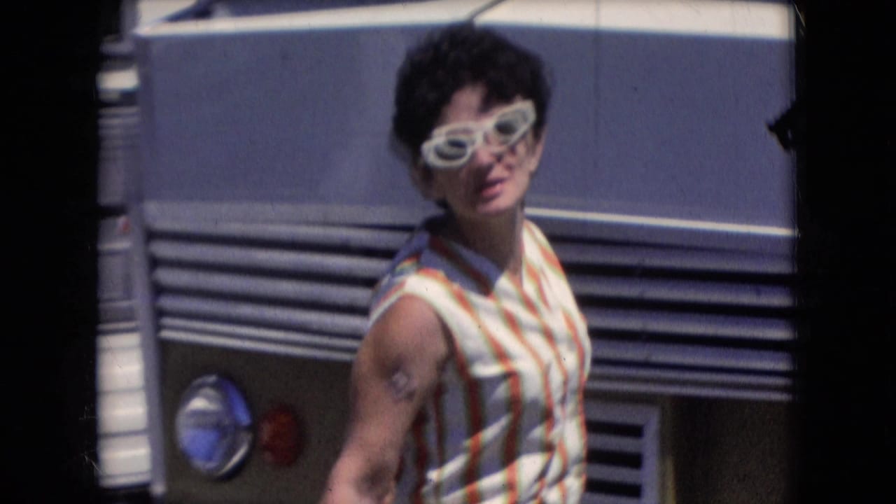 In supplied 1966 Athens, Ohio footage, a woman wearing white sunglasses and a striped sleeveless dress stands in sun beside a mobile home.