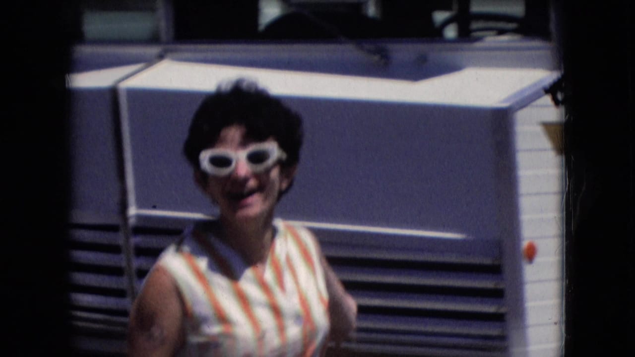 Smiling woman in white sunglasses standing in front of a mobile home.