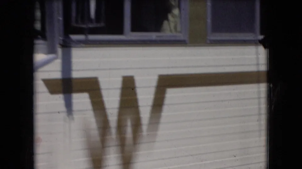 A close exterior view shows the mobile-home side, window, siding, and a large painted or shadowed marking across the paneling.