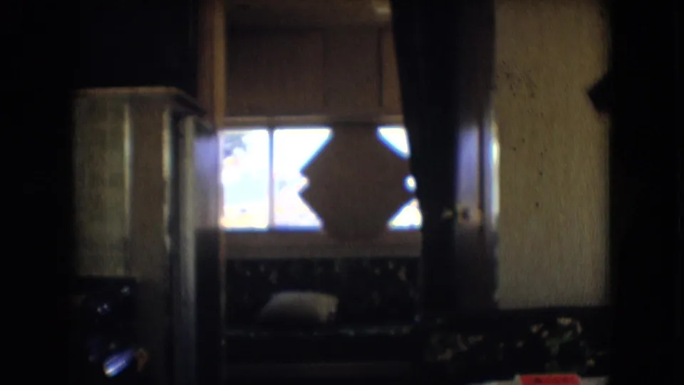 Dim 1966 home-movie view inside a motorhome in Athens, Ohio, showing a window with an X-shaped frame detail and a cushioned bench seat.
