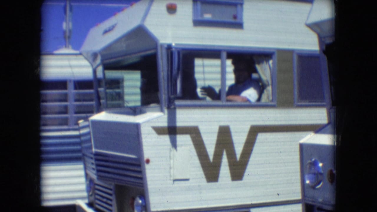 White Winnebago motorhome exterior with large W logo and driver visible in the cab window.