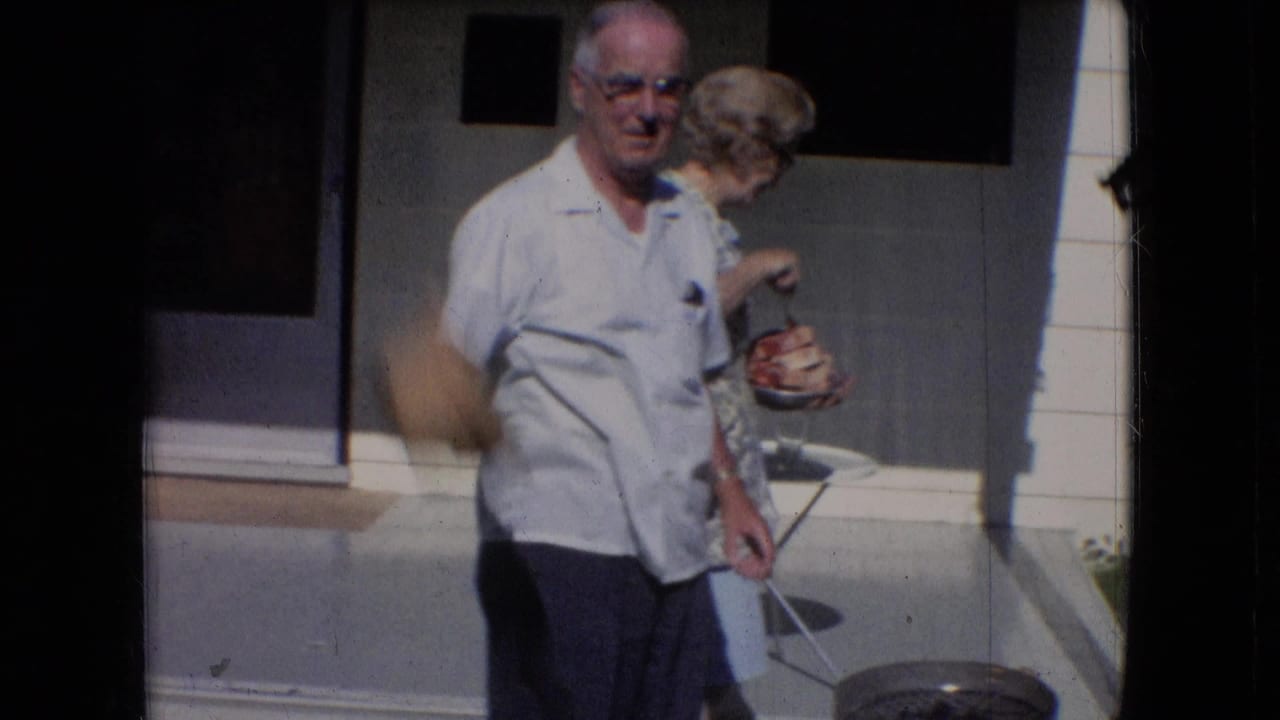 In supplied 1966 Athens, Ohio home-movie footage, an older man in a white short-sleeve shirt stands near a porch as an older woman in glasses turns beside him.