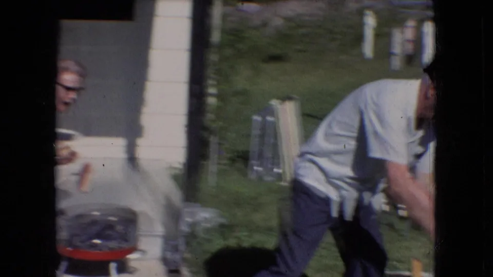 In the backyard barbecue scene, the older man bends toward a small red grill while the older woman is partly visible near the porch side of the frame.