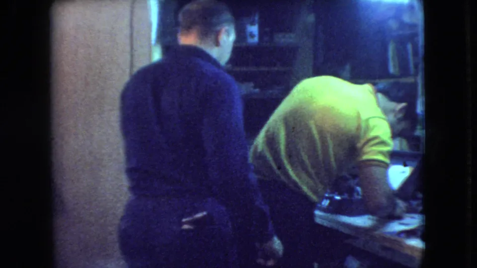 At the end of the Athens, Ohio workshop clip, two adult men stand with their backs or profiles to the camera while looking down at the workbench.