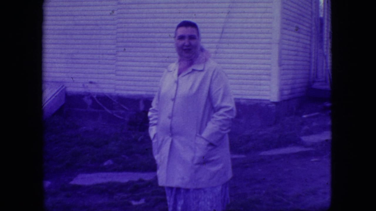 Woman in a light jacket stands outside beside a house.