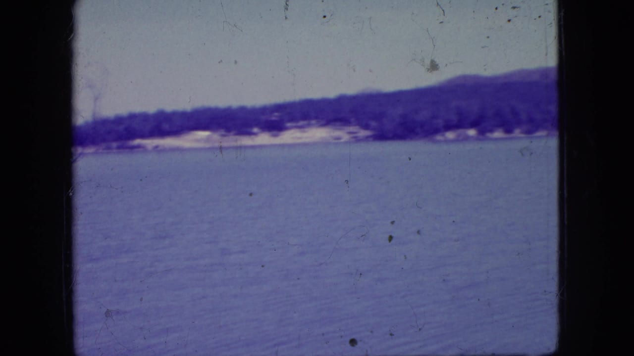Open lake surface with a far wooded shoreline and low hills under a pale sky.