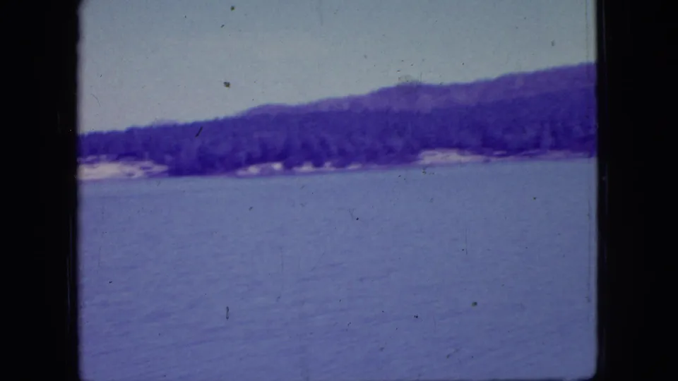 Final sampled frame from the 1966 New Jersey 8mm lake clip, showing calm water, a wooded far shore, low hills, and visible archival film wear.