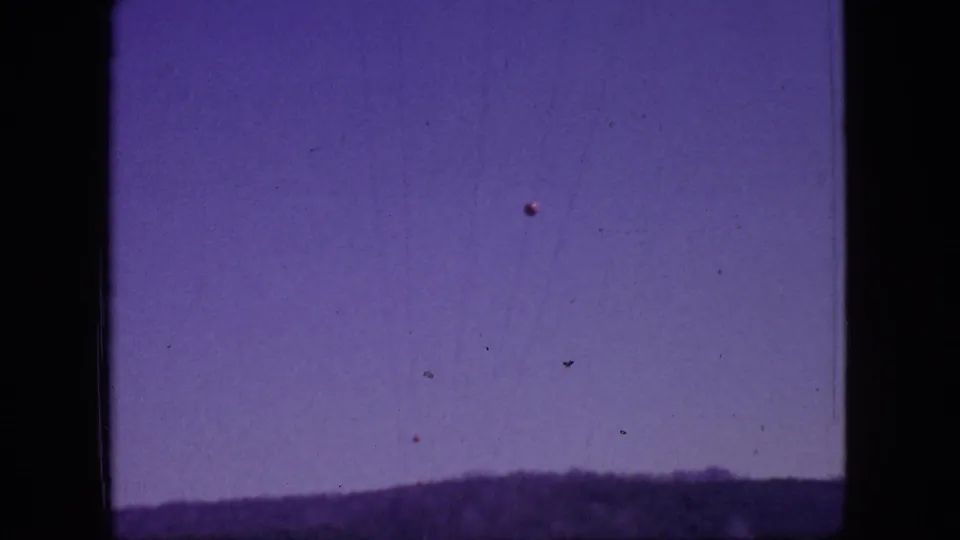 1966 New Jersey home-movie frame showing a low forested horizon beneath a large pale purple sky, with soft focus and visible film specks.
