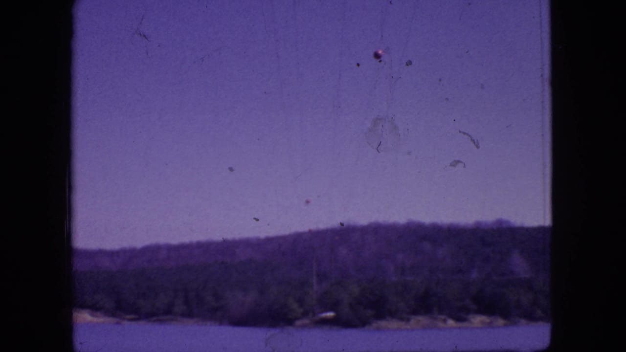 1966 New Jersey 8mm frame showing a lake, distant tree-covered hills, hazy purple-blue sky, and dark film borders.