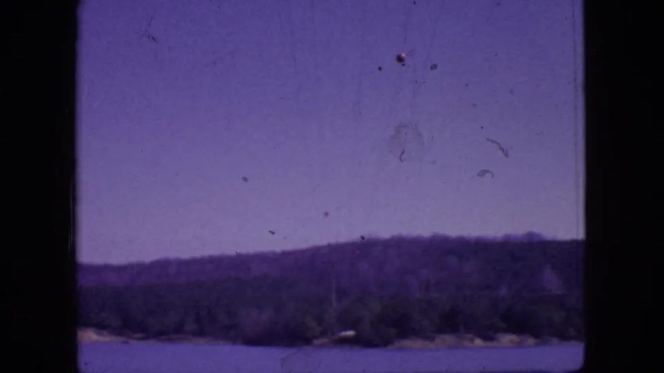 1966 New Jersey 8mm frame showing a lake, distant tree-covered hills, hazy purple-blue sky, and dark film borders.