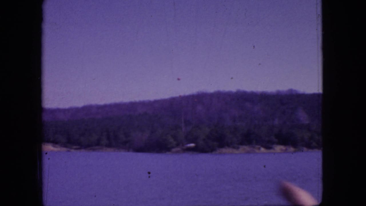 Wooded lake horizon with a hand entering at the lower right edge.